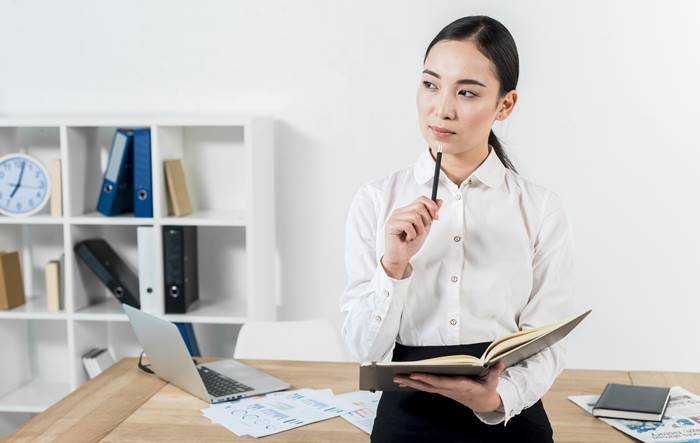 asian woman holding a notebook while thinking