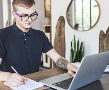 man writing while looking at his laptop