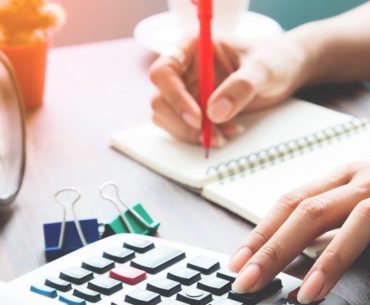 woman using calculator while taking down notes