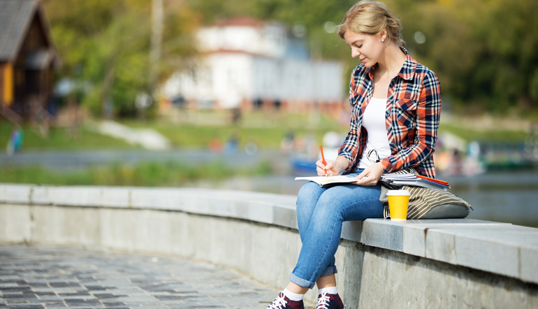 attractive student girl sitting at bridge writing