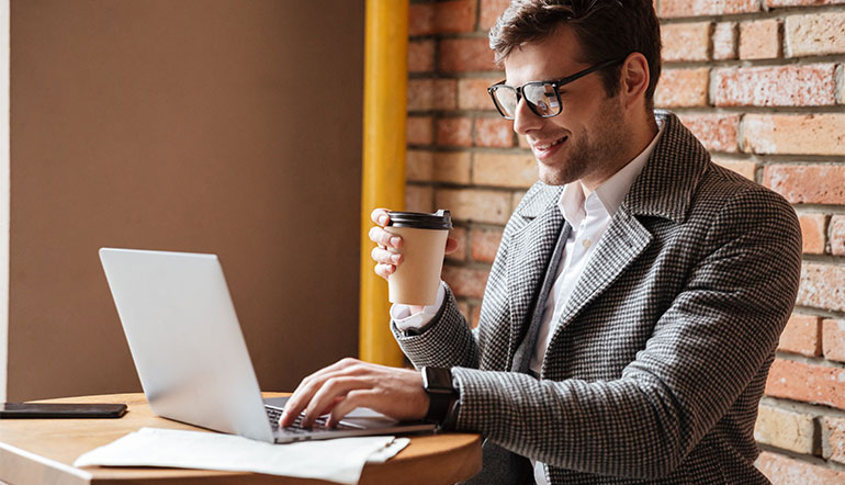 Man reading notes on laptop and drinking coffee