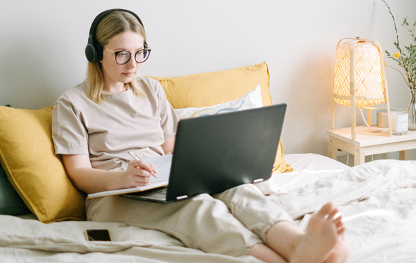 photo-of-woman-sitting-on-bed-while-using-black-laptop