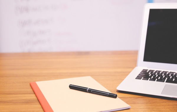 notebook with black pen and a laptop on top of the table