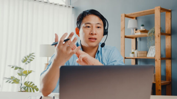 Young asia businessman wear headphones using laptop talk to colleagues