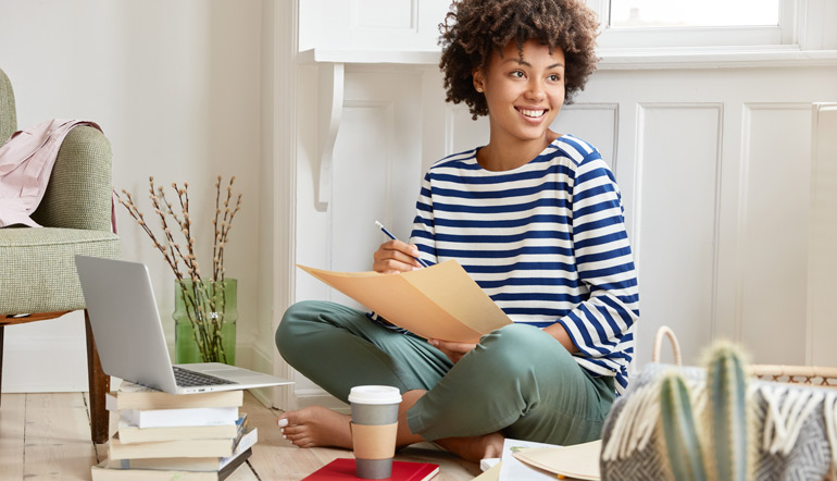 Positive black woman sits crossed legs, dressed in striped sailor sweater