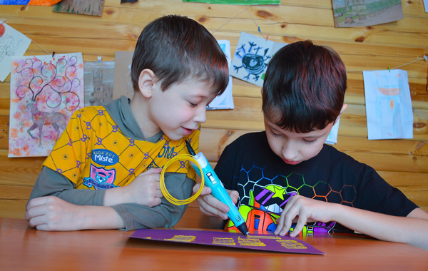 boy watching another boy draw on a purple piece of paper