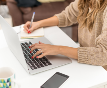 woman taking down notes while using laptop