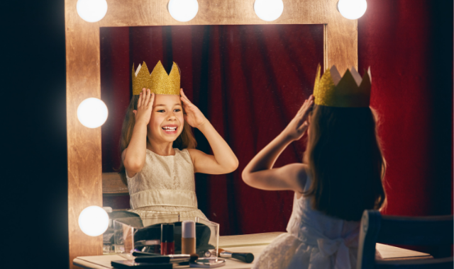 little girl facing a vanity mirror holding a crown