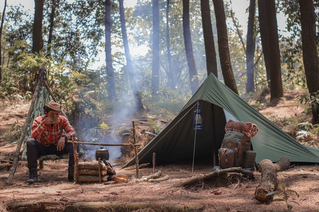 man in forest seated outside tent