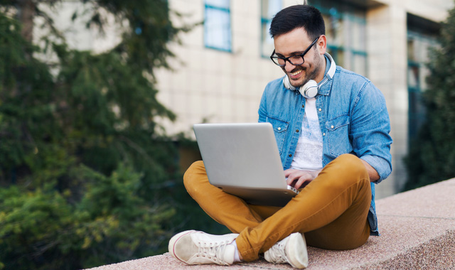 cheerful man working outside using his laptop