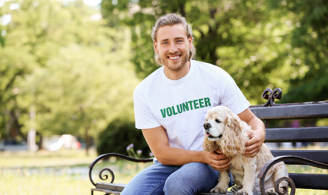male volunteer with dog sitting on bench outdoors