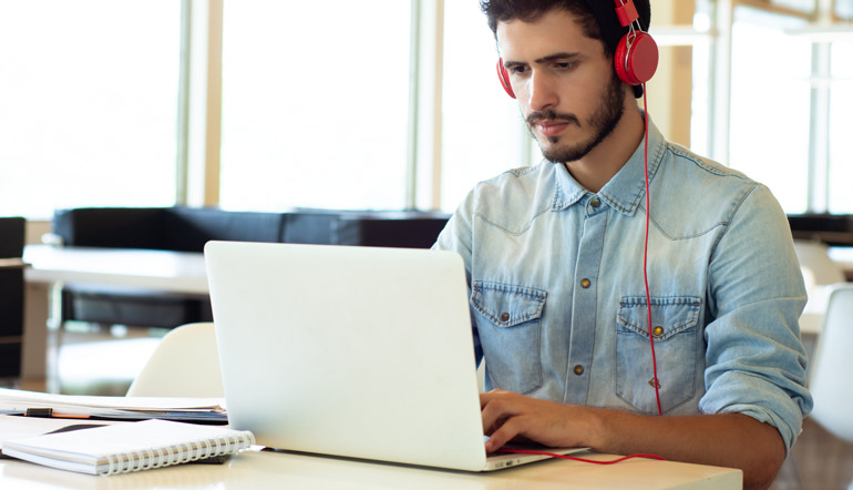 male with red headphone using laptop