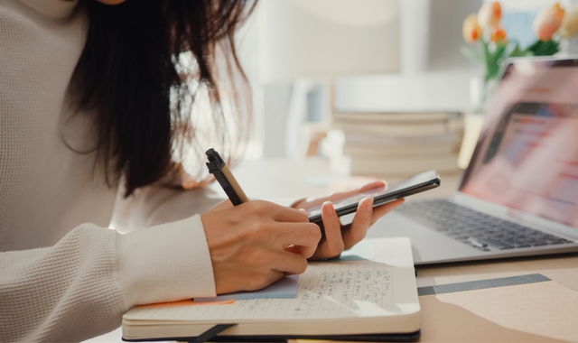 woman holding phone and taking notes