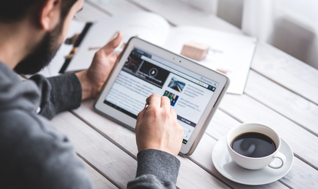 man reading intently on a tablet with a cup of coffee beside him