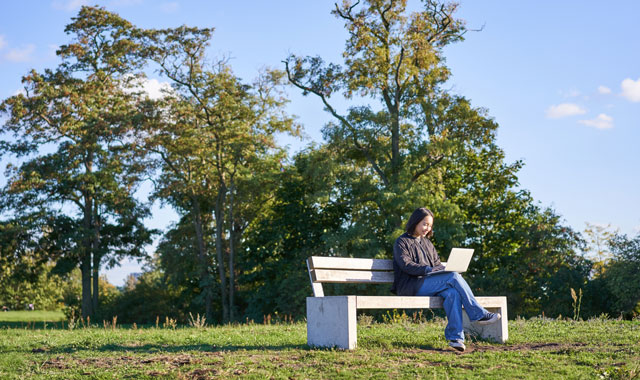 woman using laptop sitting in park on bench typing on computer