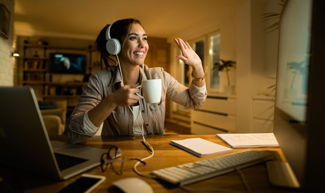 happy woman drinking tea and waving to someone while having video