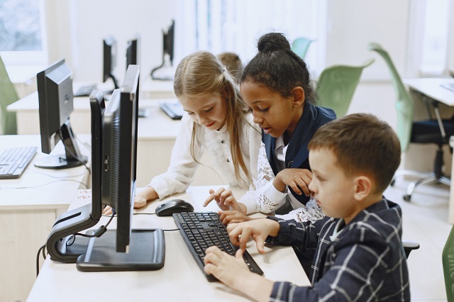 three middle-school-aged kids coding in a computer lab