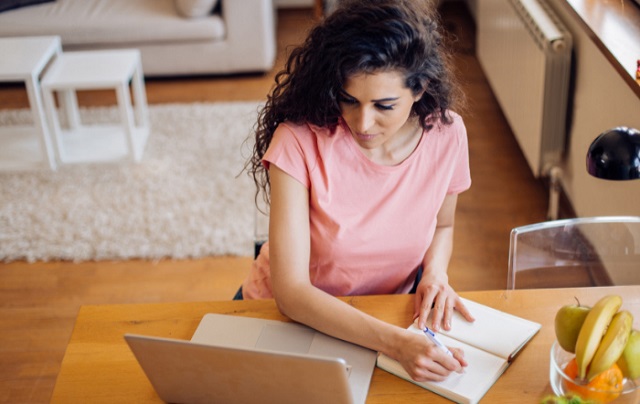 lady writing on a notebook while looking at a laptop